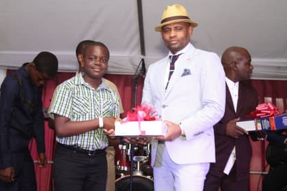 A NY Chapter representative presenting a gift to a smiling young Glenmuir student on stage