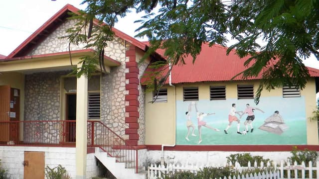 A stone-fronted school building with a red roof and a mural of students playing football
